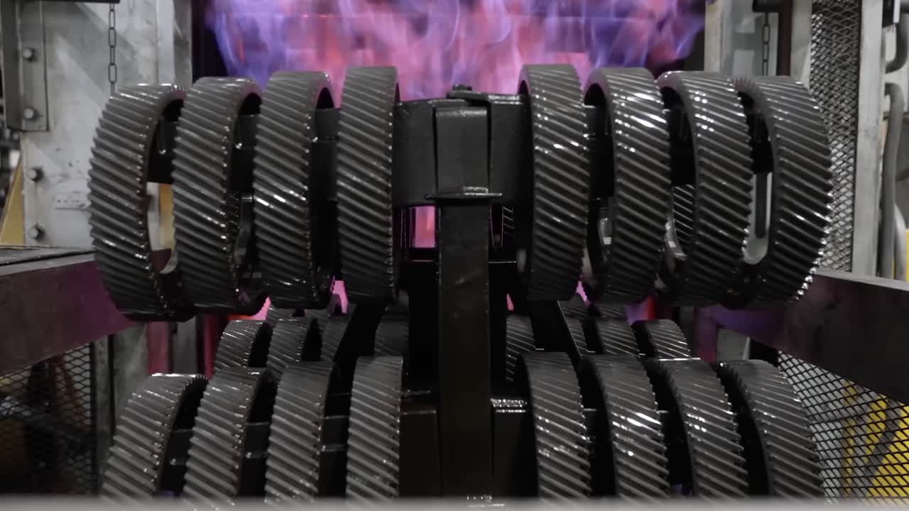 Front view of industrial helical gears emerging from a high-heat quenching furnace surrounded by intense atmospheric flames