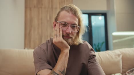 a tired blond man with a beard and glasses covered himself with a blanket and his little albino son pulls the blanket off him and wants to play with his father in a modern apartment at home