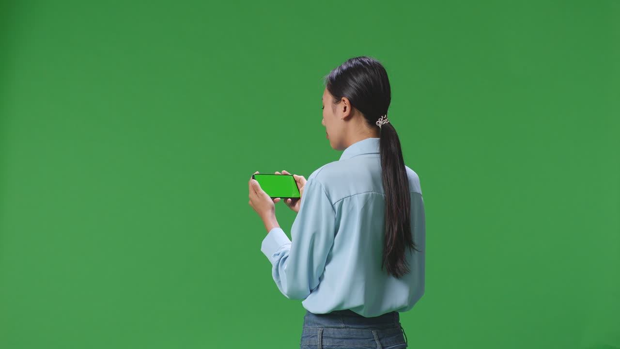 vista trasera de una mujer de negocios asiática usando un teléfono móvil con una pantalla verde simulada en el fondo de la pantalla verde en el estudio