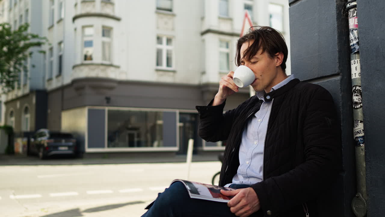 En ung mand nyder et stille øjeblik i byen, nipper til kaffe og læser et magasin, fanget i et filmisk nærbillede, der afspejler afslappet elegance og moderne livsstil