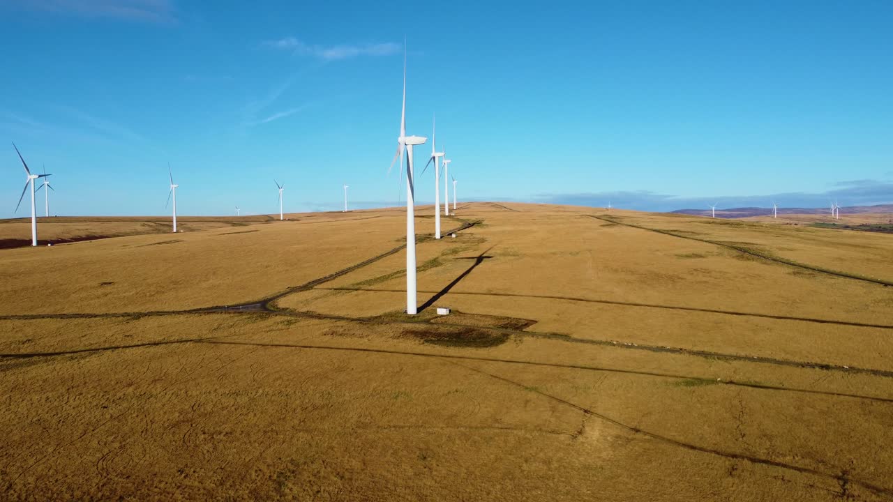 Slow Rising Aerial of Wind Turbines Over Natural Landscape with Blue Sky Background. Alternative Sustainable Energy Industry in Natural Environment