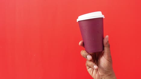 person holding a coffee cup in front of a red background