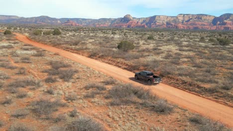 a 60fps drone shot following black ford f250 driving on a red dirt road in the desert near sedona with striking mountains in the background