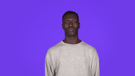 portrait of young serious man staring at camera with crossed arms protesting. beautiful african black man in white sweatshirt on blue background