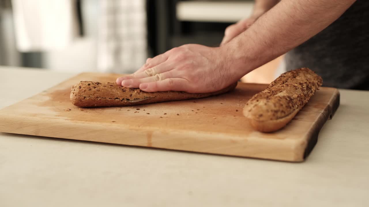 Man slicing healthy baguette on wooden chopping block on the kitchen countertop