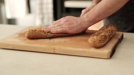 man slicing healthy baguette on wooden chopping block on the kitchen countertop