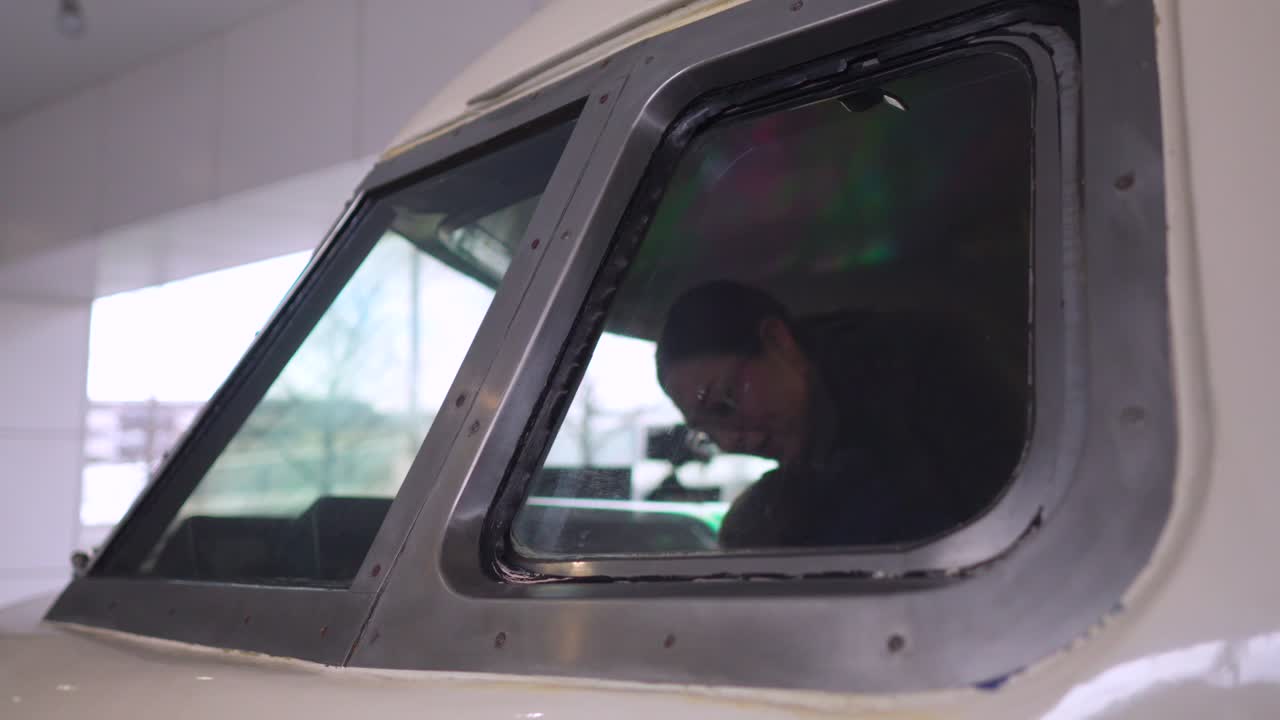 Eine weiße lateinamerikanische Mutter und ihr Baby lachen fröhlich im Führerstand einer alten Lokomotive, von außen durch das Fenster gesehen, während ihres Besuchs im Kyoto Eisenbahnmuseum in Japan