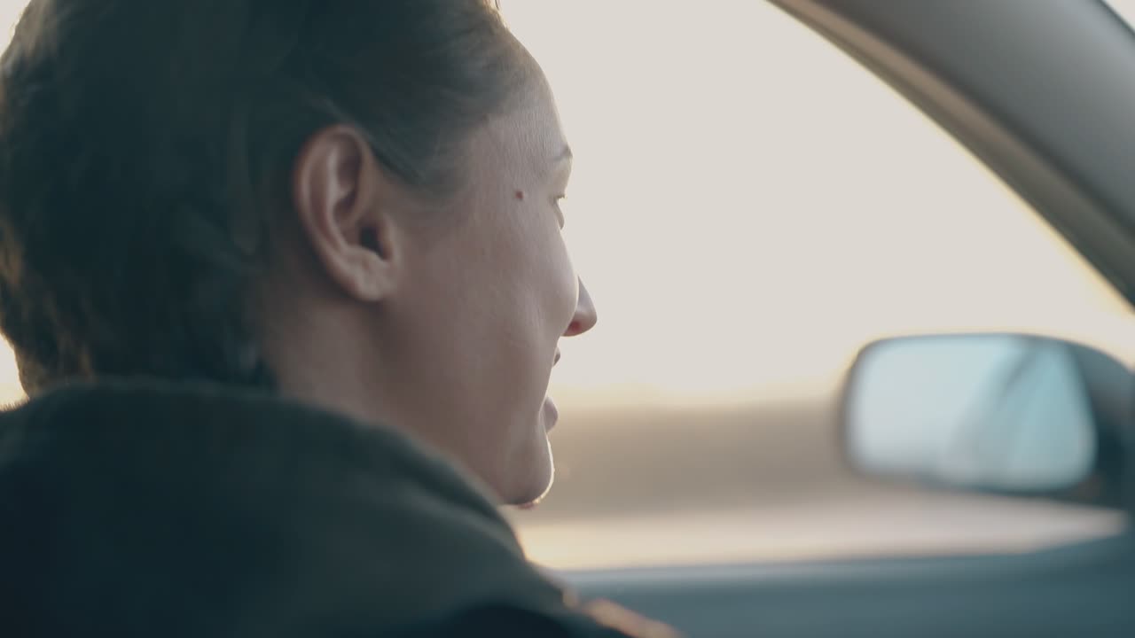 어두운 머리카락과 머리 ⁇ 을 가진 젊은 여성이 차에 앉아서 이야기합니다.