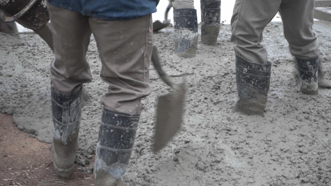 A group of workers with their boots on wet concrete paving a road.