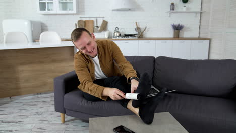 man cleaning socks at home. young man brushes his socks with a brush while sitting on a couch during quarantine.