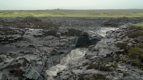 Río-Glacial-Que-Fluye-A-Través-De-Roca-Volcánica-Negra-En-Un-Día-Sombrío