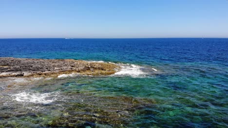 Vista-Aérea-Hacia-Adelante-De-Las-Olas-Salpicando-La-Playa-Azul-Esmeralda-De-Piedra-Caliza-Rocosa-En-Sliema,-Malta