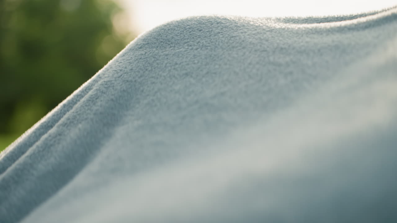 Close up young girl smiling with joy as blanket covers head and sways hair, sunlight backlighting strands, green blurred park background, carefree summer moment, joyful bonding moment