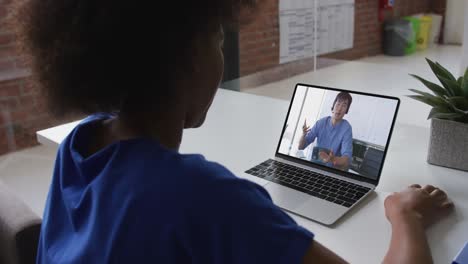 Back-view-of-african-american-woman-having-a-video-call-with-male-colleague-on-laptop-at-office