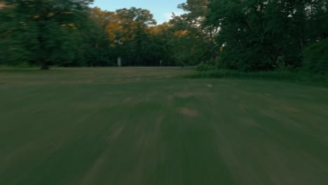 high speed drone flight across lush green grass and trees followed by vertical ascent to a breathtaking panoramic view over a forest at sunset