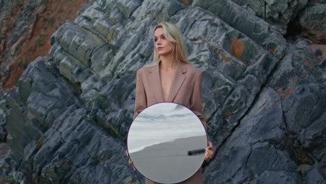 seashore girl posing rocks zoom on. serious attractive lady holding round mirror