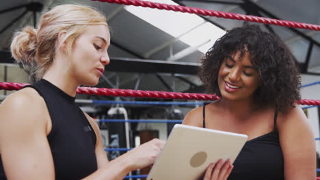 Female-Personal-Trainer-With-Female-Boxer-In-Gym-Checking-Performance-Using-Digital-Tablet