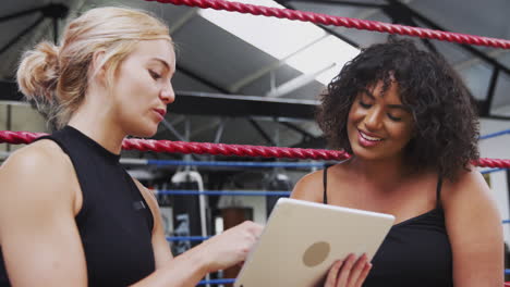 female personal trainer with female boxer in gym checking performance using digital tablet