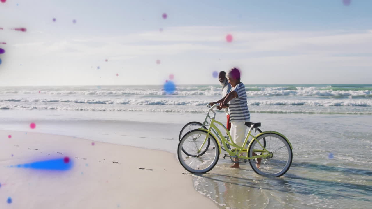 Elderly couple walking bicycles along beach with colorful dots animation overlay