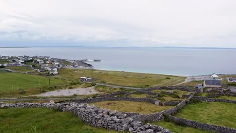 rising drone shot of inisheer or inis oirr aran islands showing the stone walls that divide fields and the inis oirr ferry birthed in the harbour reminiscent of scenes in banshees of inisherin