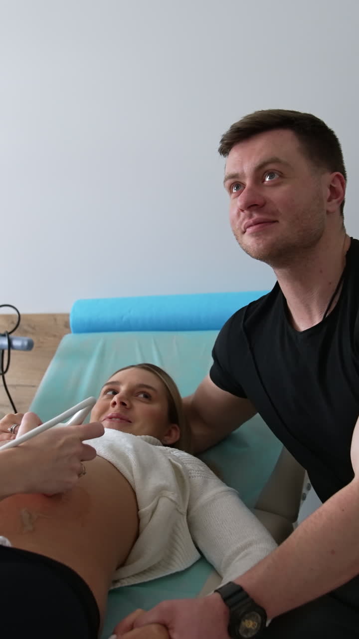 Happy future parents look at the screen showing their unborn baby. Couple at the ultrasound examination of a child development. Vertical video