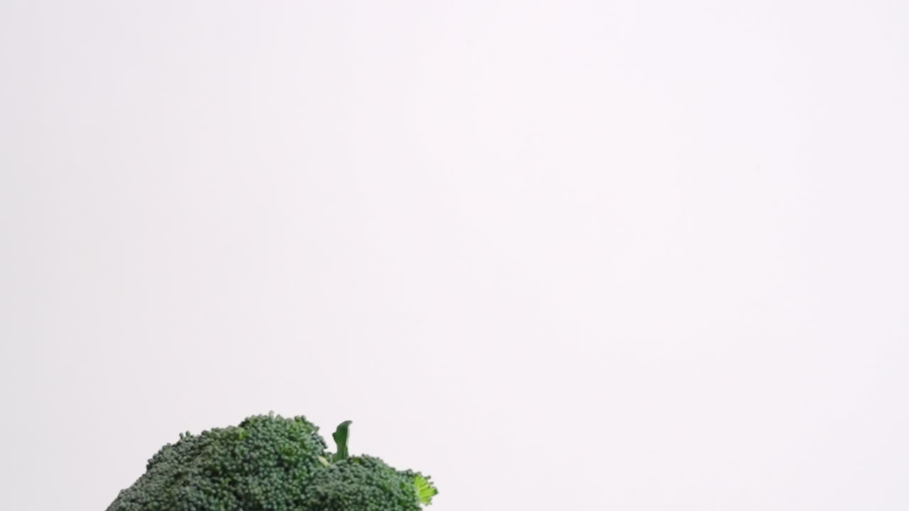 Testa intera di broccolo che cade al rallentatore su sfondo bianco in 4K