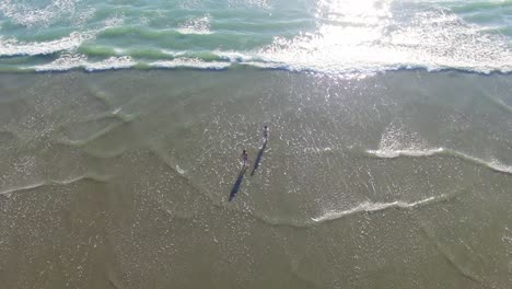 tourist enjoying the bright summer day on the beach with waves splashing to their feet during sunny day in new zeland - aerial shot
