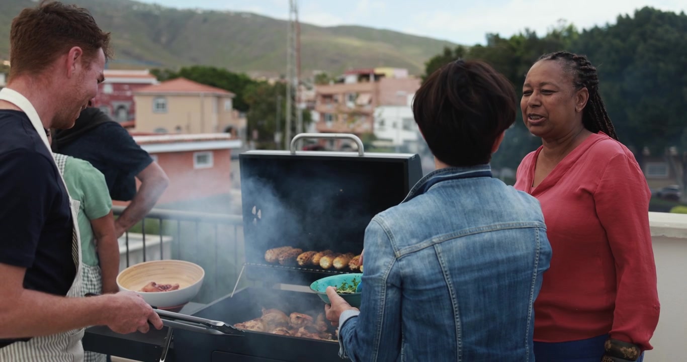 Amici multietnici felici che grigliano cibo su una terrazza panoramica