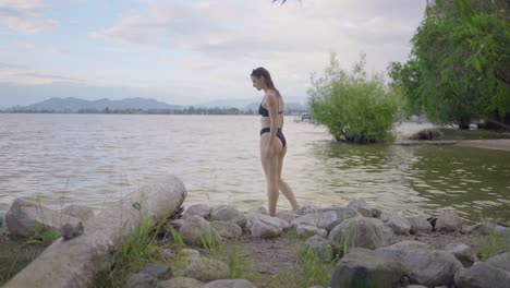 Side-view-of-attractive-girl-walking-away-on-rocky-beach