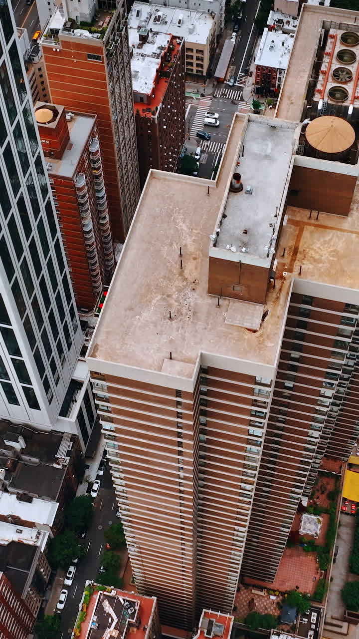 Lowering above the tops of high buildings at downtown. Numerous cars move by New York roads. Vertical video