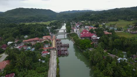 Drone-Aéreo-Vuela-Sobre-El-Río-Loboc-Filipinas-Río-Húmedo-Paisaje-De-Colinas-Verdes-Con-Un-Pequeño-Pueblo-Y-Casas-De-Tejas-Rojas