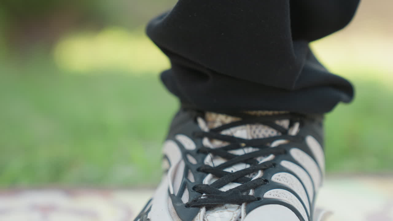 Un corridore si assicura attentamente della stabilità delle scarpe. Uno sprinter concentrato si allaccia le scarpe con calma su un terreno erboso. Il corridore fissa con attenzione le scarpe sull'erba per garantire stabilità durante una tranquilla attività di corsa.
