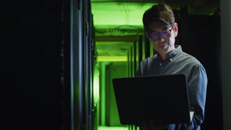 Asian-male-it-technician-using-laptop-checking-computer-server