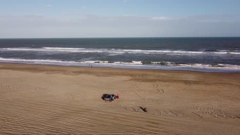 Alta-Vista-Aérea-En-órbita-De-La-Familia-Y-Tracción-En-Las-Cuatro-Ruedas-Estacionada-En-El-Lado-De-La-Playa-En-Una-Hermosa-Mañana-De-Amanecer-En-Vacaciones-En-Mar-De-Las-Pampas,-Sudamérica