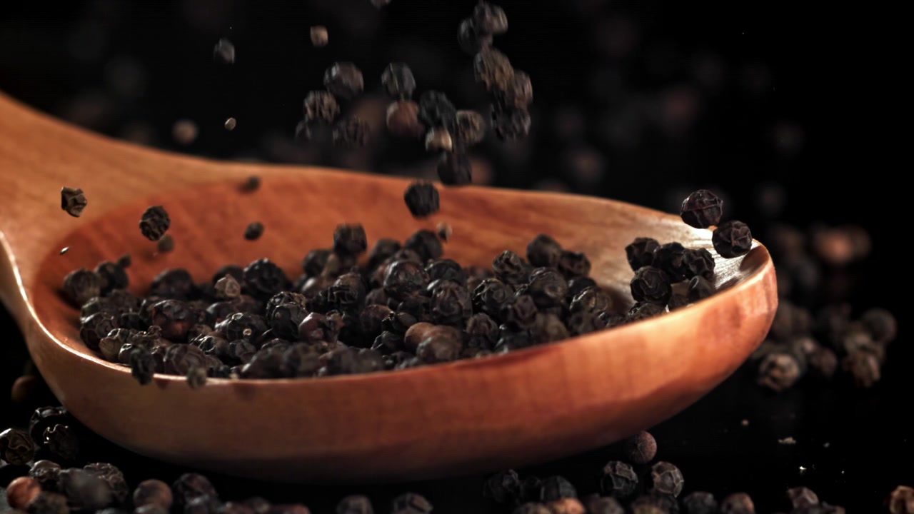 Svarte pepperkorn som faller ned i en treskje.