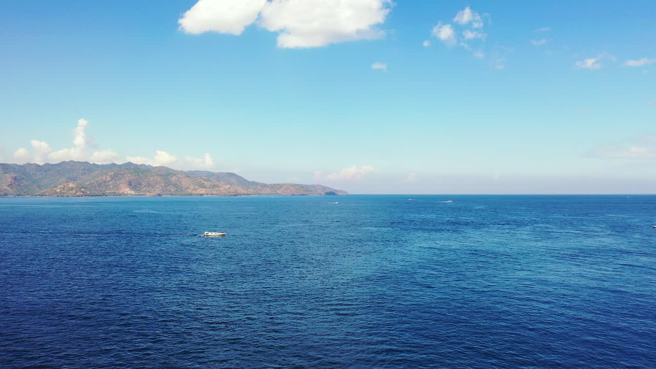 Endless blue sea surface with vibrant water reflecting bright sky with white cloud hanging over mountains of tropical islands in Bali