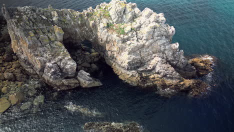 Backward-Up-Tilt-Reveals-A-Boat-Sailing-in-a-Body-of-Water-Surrounded-by-Rocky-Coastline