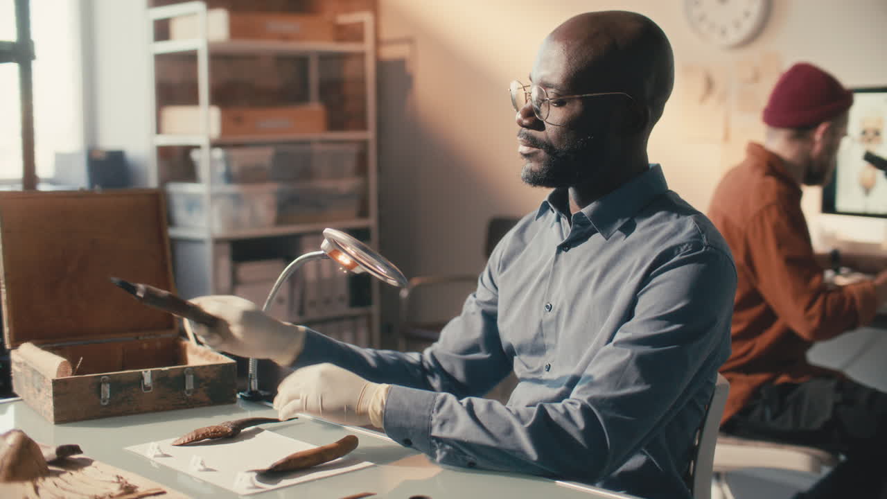 Archaeologist Examining Ancient Tools, His Colleague Using Microscope in Lab
