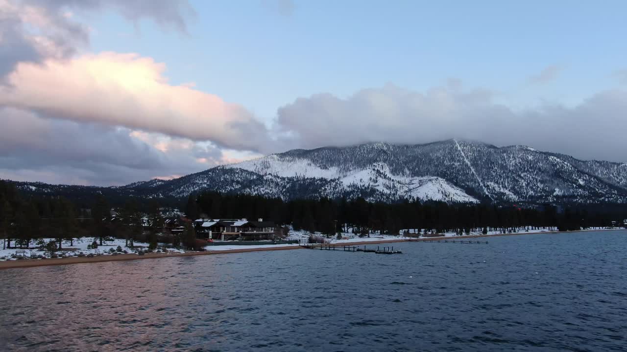 Stabilized 4K drone aerial footage shows the snowy shoreline of South Lake Tahoe, California during sunset and golden hour to reveal the beach and crystal clear waters of Lake Tahoe with bright colors