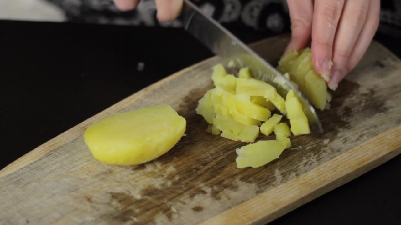 Cutting boiled potato in small pieces with knife, static high angle