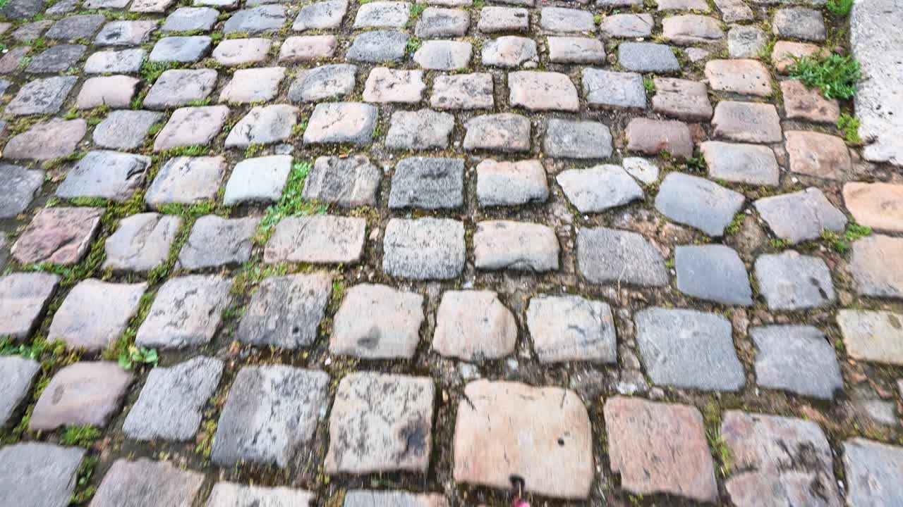 Handheld camera movement over uneven granite cobblestones on an ancient European village street