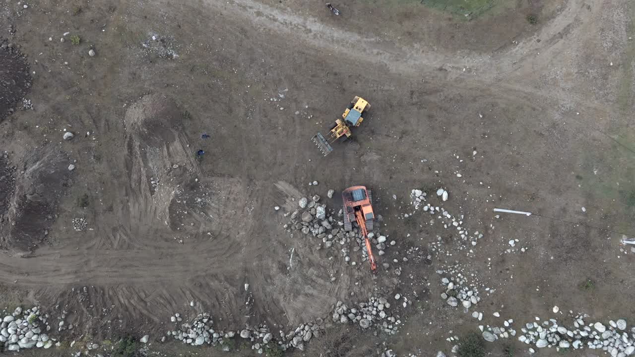 vista aérea de arriba hacia abajo de dos excavadoras retro, una amarilla y la otra naranja, trabajando en terreno rocoso