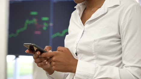 En-El-Ajetreo-De-La-Oficina,-Una-Mujer-Negra-Concentrada-Gestiona-Las-Transacciones-En-Su-Teléfono