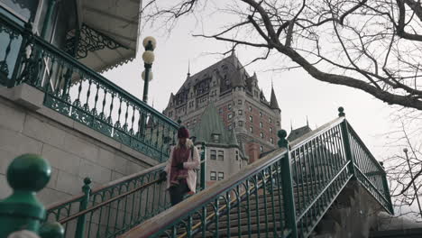 mujer sonriente bajando las escaleras frente al chateau frontenac en la ciudad de quebec, canadá - tiro de ángulo alto