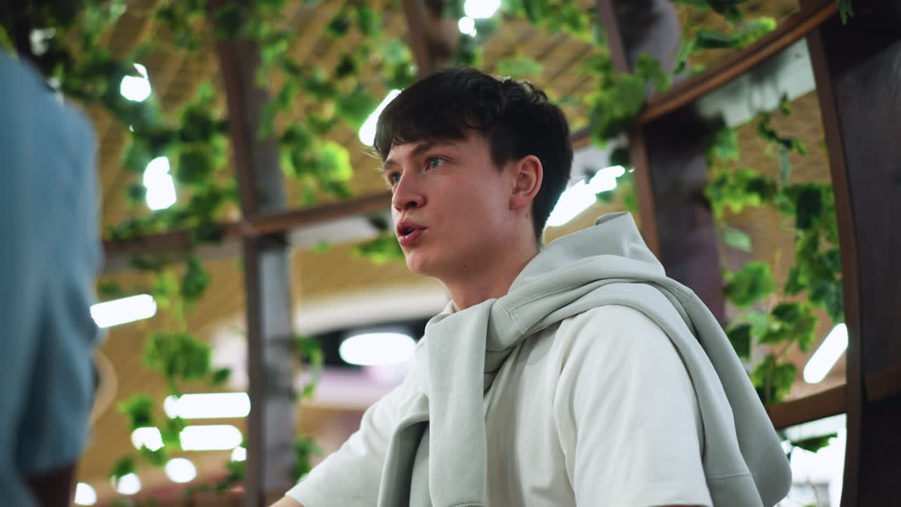 under view of European man talking while adjusting sweater around neck near transparent walls, camera capturing candid expression and movement, modern interior reflected in glass panels