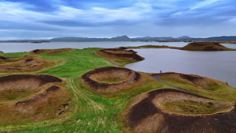 meadow with crater holes and paths around them. waterscape surrounding the picturesque landscape. dramatic cloudscape in the sky of iceland.