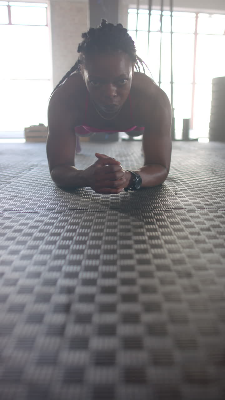 Vertical video: Planking on gym floor, woman focusing on core strength and fitness training