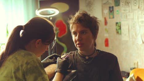young woman talking to tattoo artist applying ink to her skin