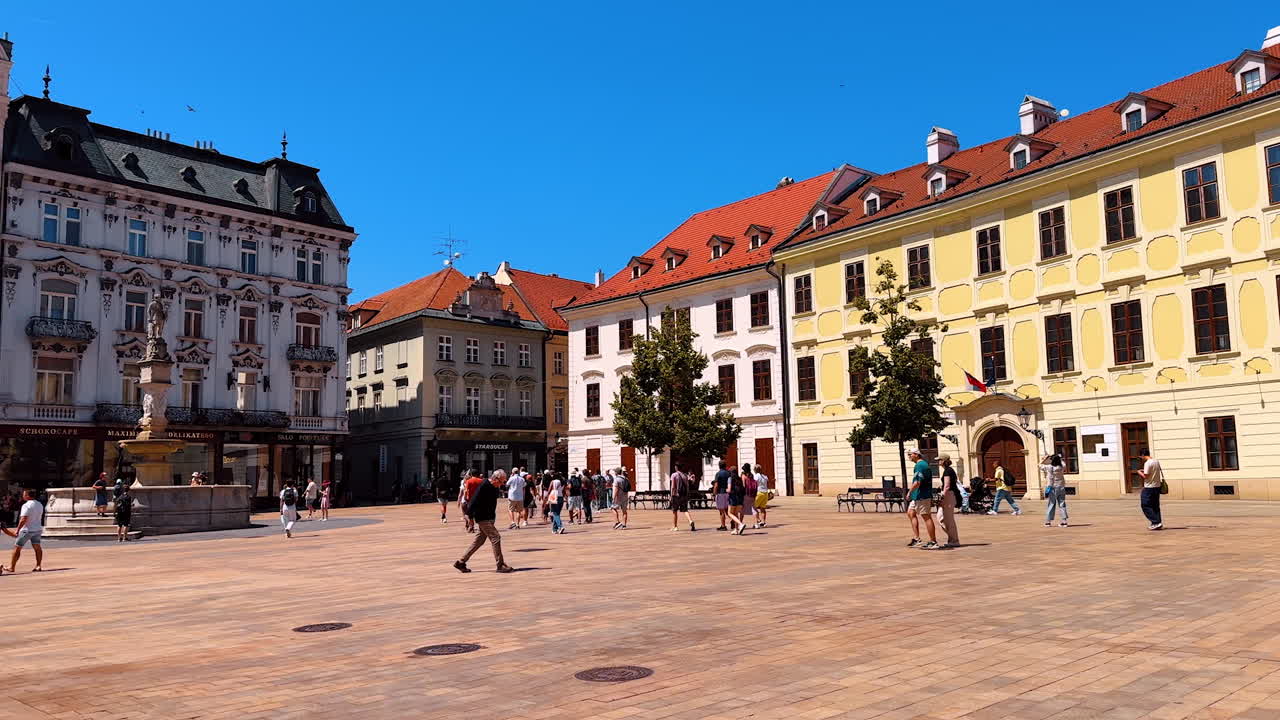 People walking by the square surrounded by the gorgeous architecture. Tour by the old town in Bratislava, Slovakia in summer