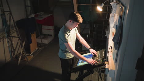 young technician operates control panel under focused light in backstage area filled with cables, ladders, and bulletin board. scene captures concentrated atmosphere of technical work in dim industrial space